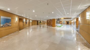 Un amplio vestíbulo de hotel con techo alto, pisos de mármol pulido y una escalera central que conduce a un nivel superior.