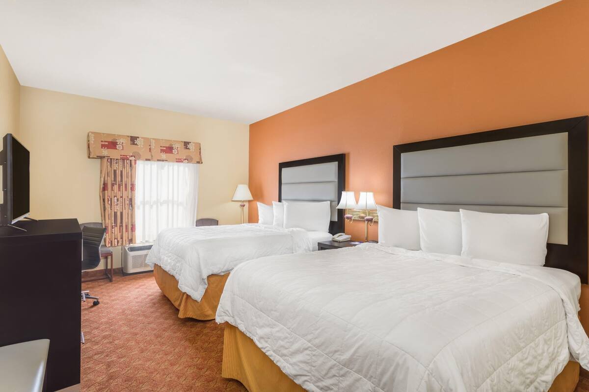 A hotel room with two beds, a desk, a chair, and a television.