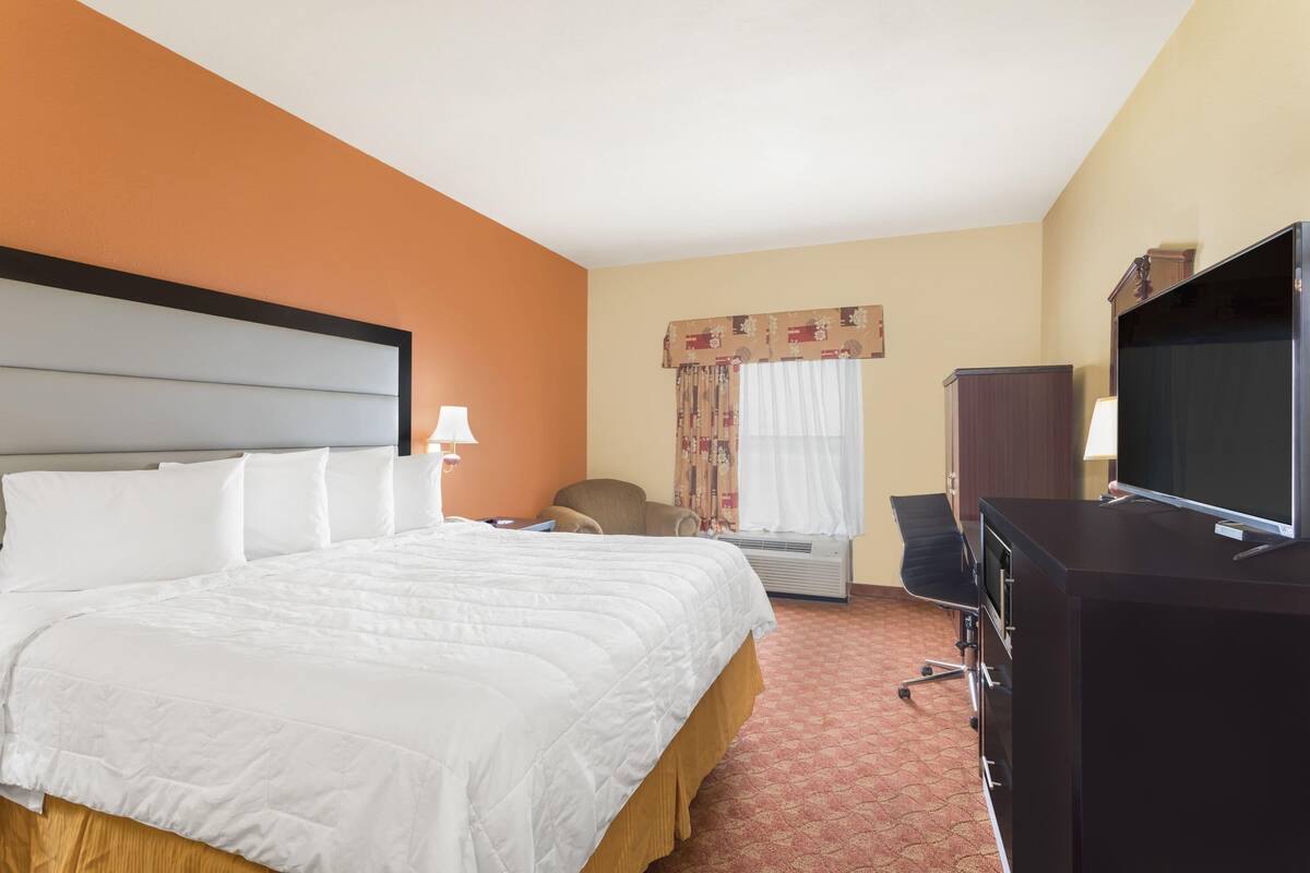A hotel room with a large bed, a desk with a computer, a television, and a window with curtains.