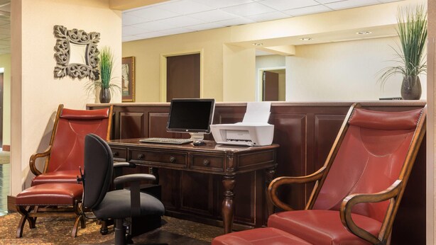 Un hall de hotel con una recepción, dos sillones de cuero, una computadora e impresora.
