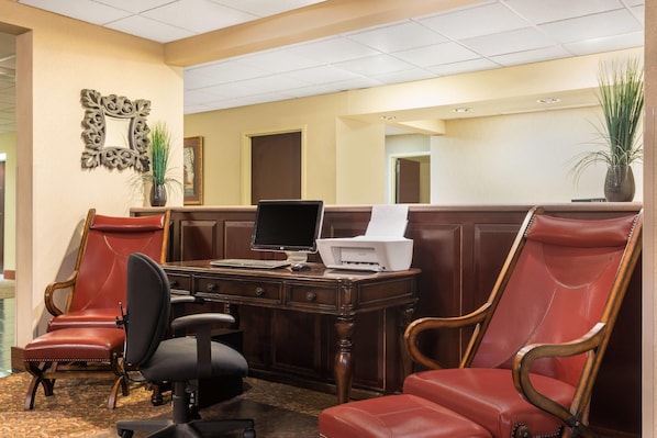 Un hall d’hôtel comprenant un comptoir d’accueil, deux fauteuils en cuir, un ordinateur et une imprimante.