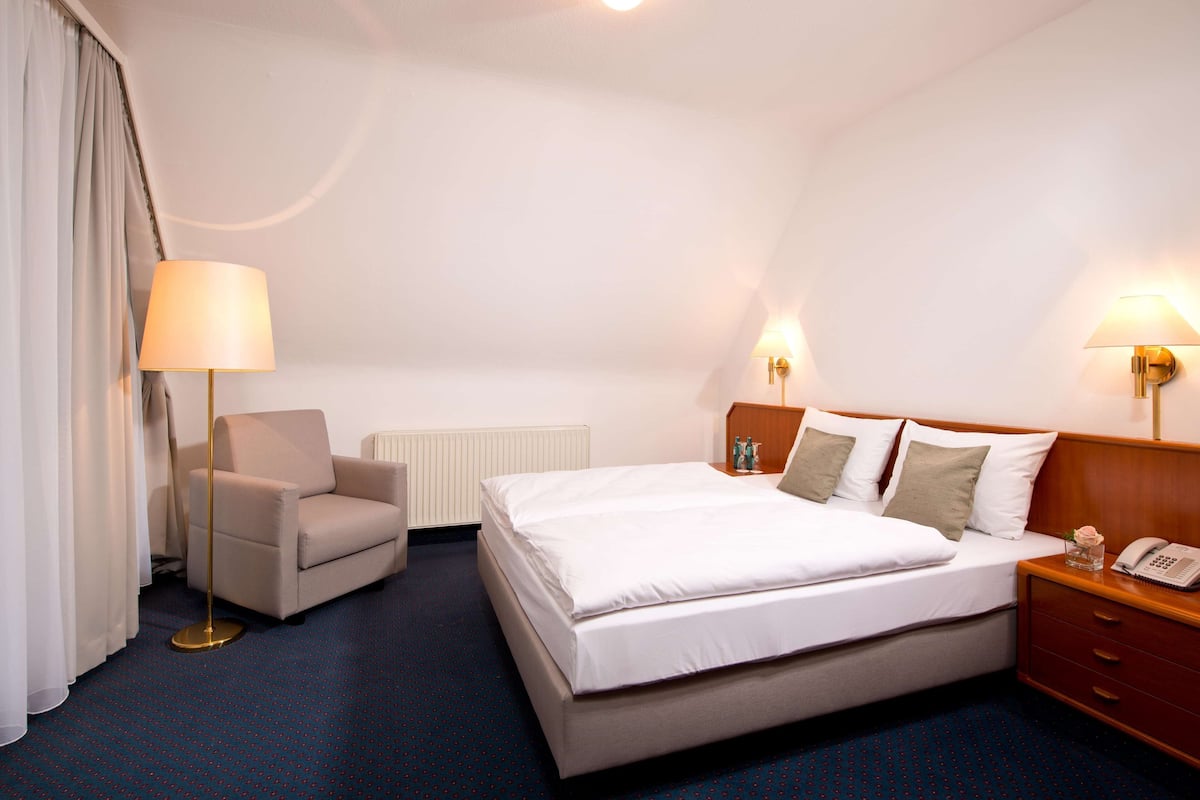Une chambre d’hôtel avec un lit, une chaise, un bureau avec une lampe et un téléphone.
