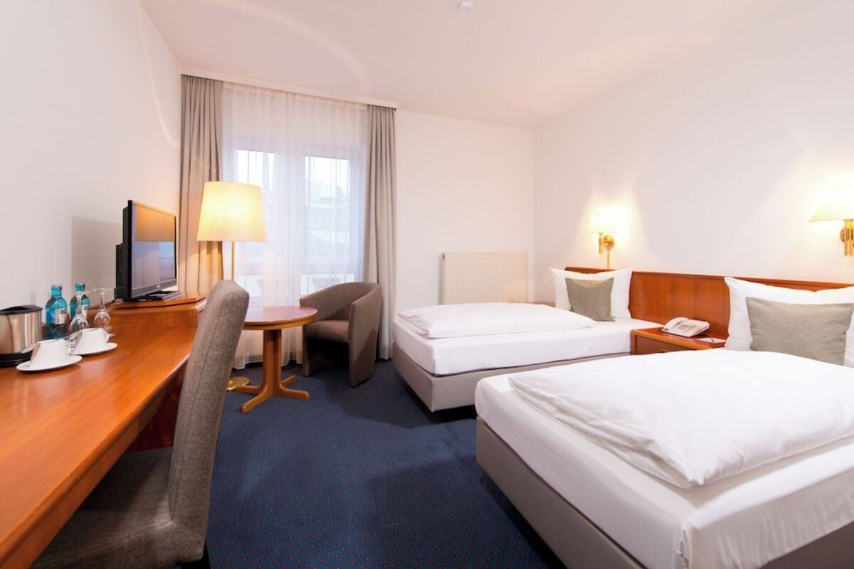 Une chambre d’hôtel équipée d’un bureau, de deux lits, d’une chaise, d’un téléviseur et d’une lampe.