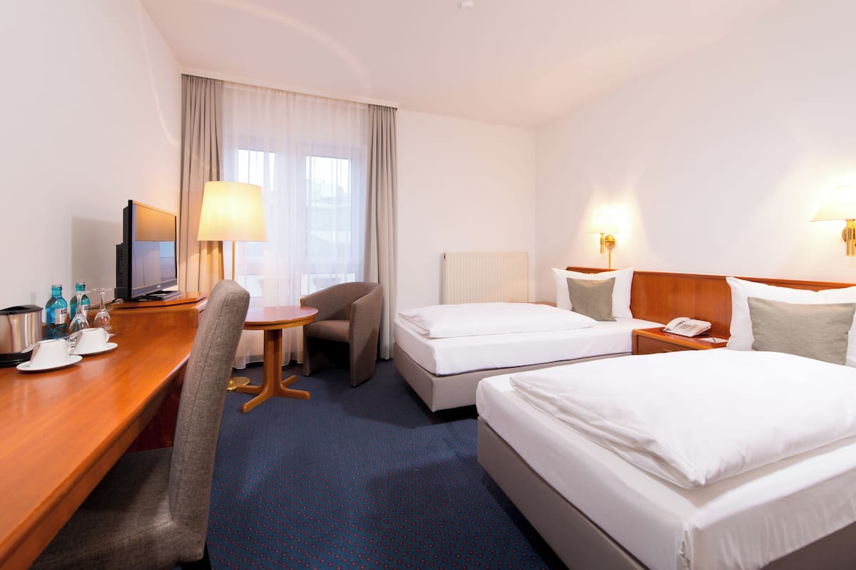 Une chambre d’hôtel équipée d’un bureau, de deux lits, d’une chaise, d’une télévision et de lampes.