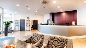 A modern hotel lobby with a reception desk, seating area, and a large plant. - ACHAT Hotel Neustadt an der Weinstraße (Neustadt an der Weinstrasse)