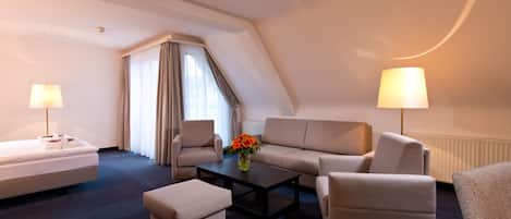 Habitación de hotel con cama, dos sillones, un sofá, una mesa de centro y dos lámparas.