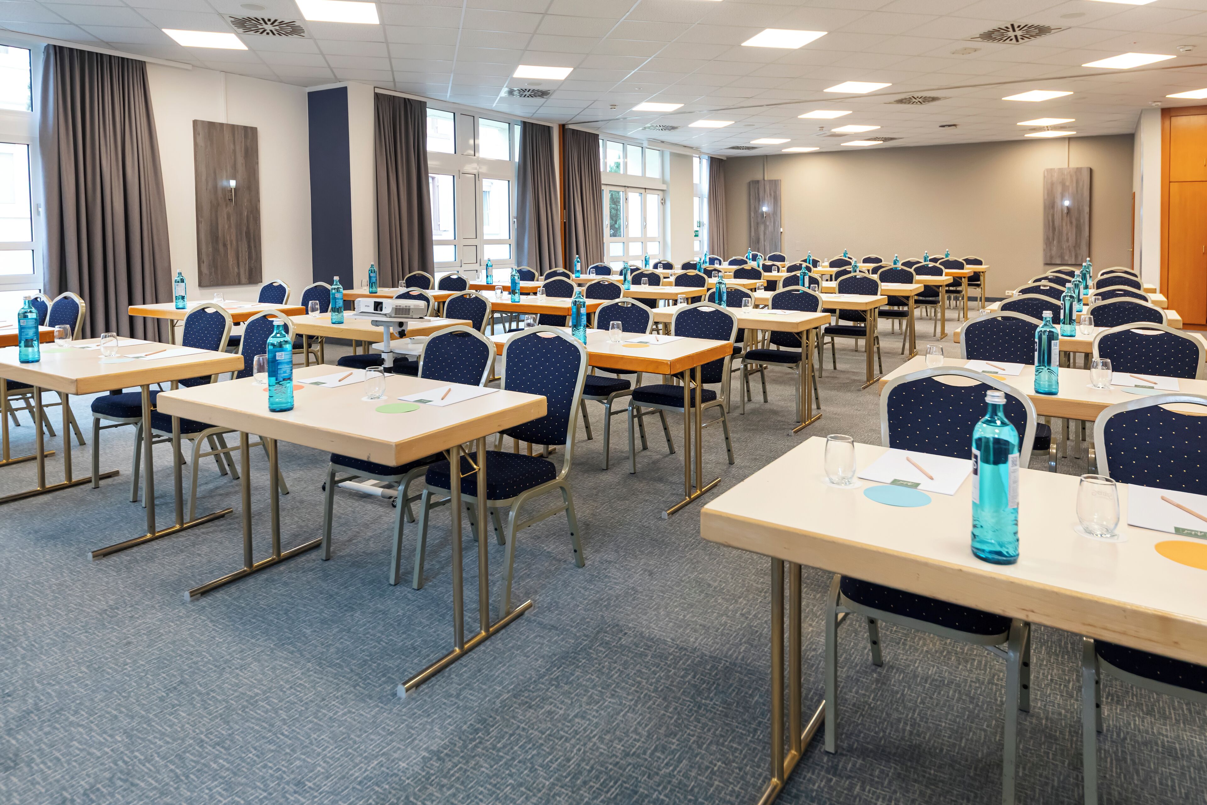 A conference room with multiple tables and chairs, equipped with water bottles and documents.