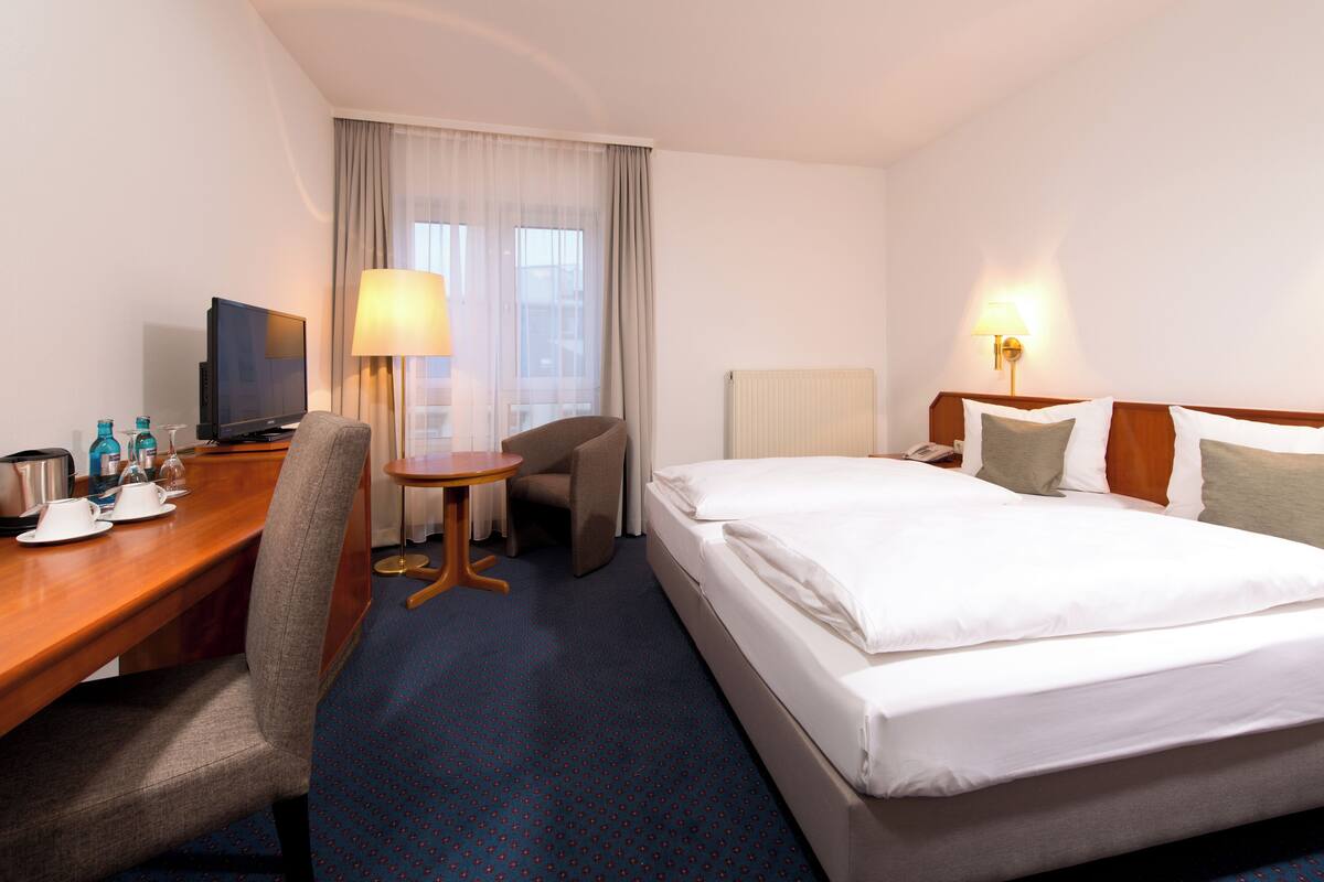 Une chambre d’hôtel comprenant un lit, un bureau avec une télévision, une chaise, une petite table et deux lampes.