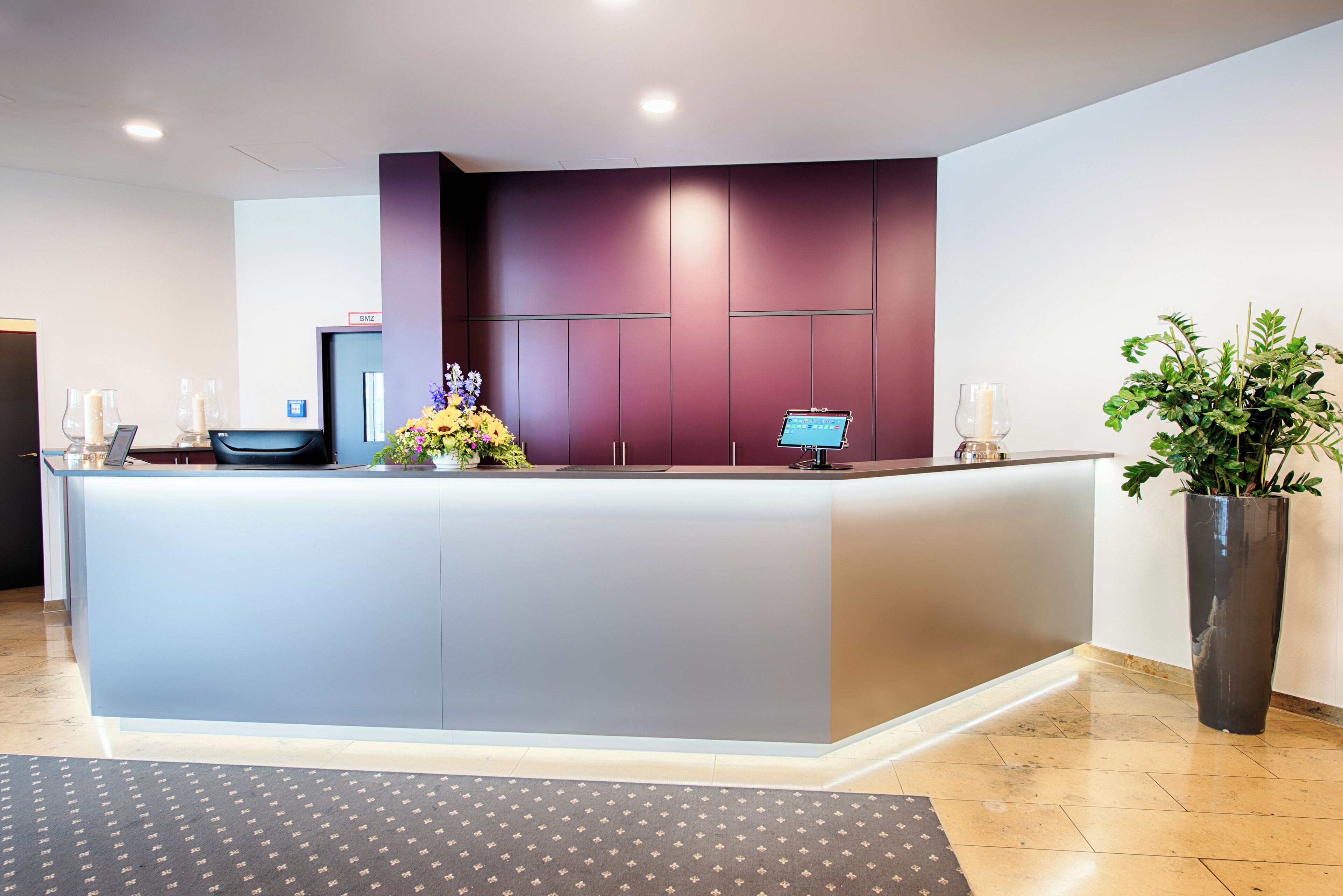 A reception area with a marble counter, a computer, and a potted plant.