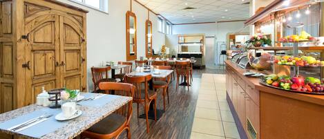 Un comedor de hotel con armarios de madera, mesas con cubierta de mármol y un bufé de frutas y verduras.