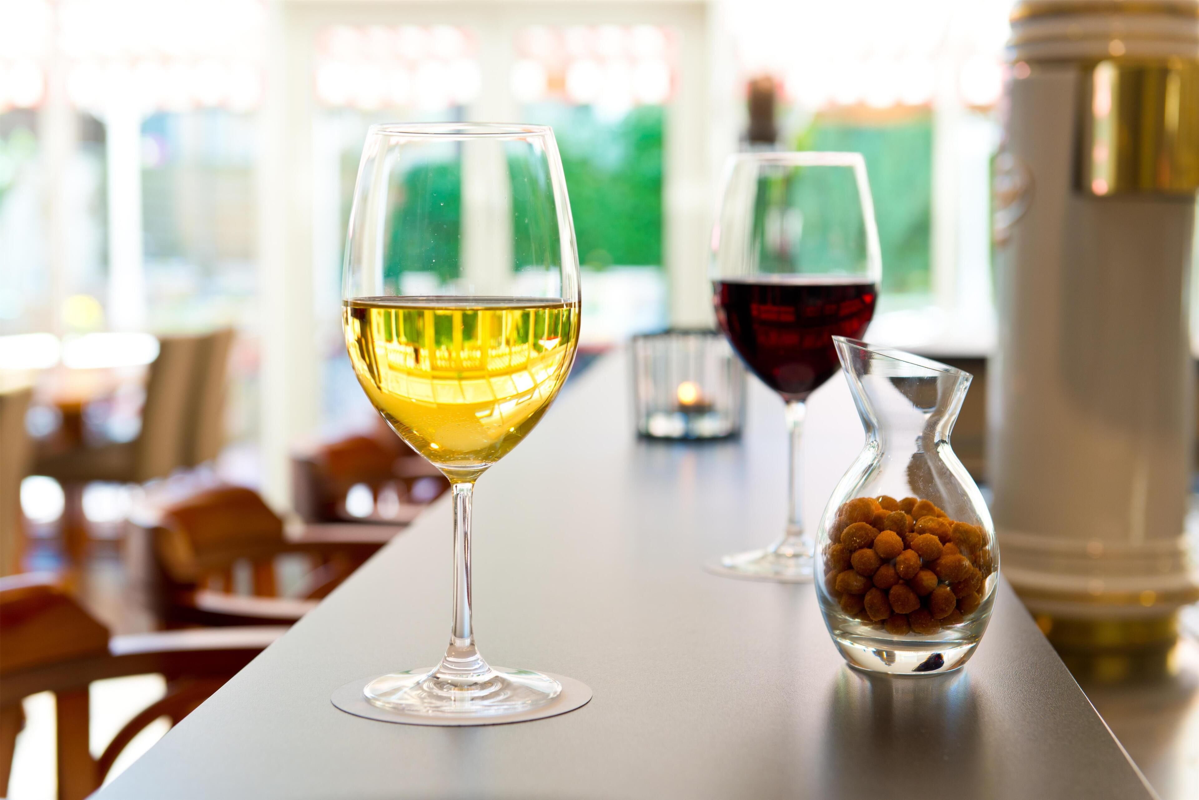 A bar setting with two glasses of wine and a small glass container of nuts.