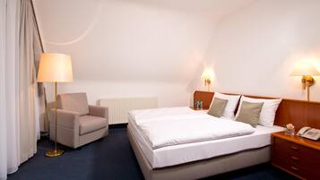 Habitación de hotel con cama, una silla, mesita de noche con lámpara y teléfono.