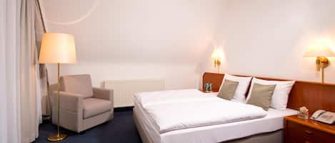 Habitación de hotel con cama, una silla, mesita de noche con lámpara y teléfono.