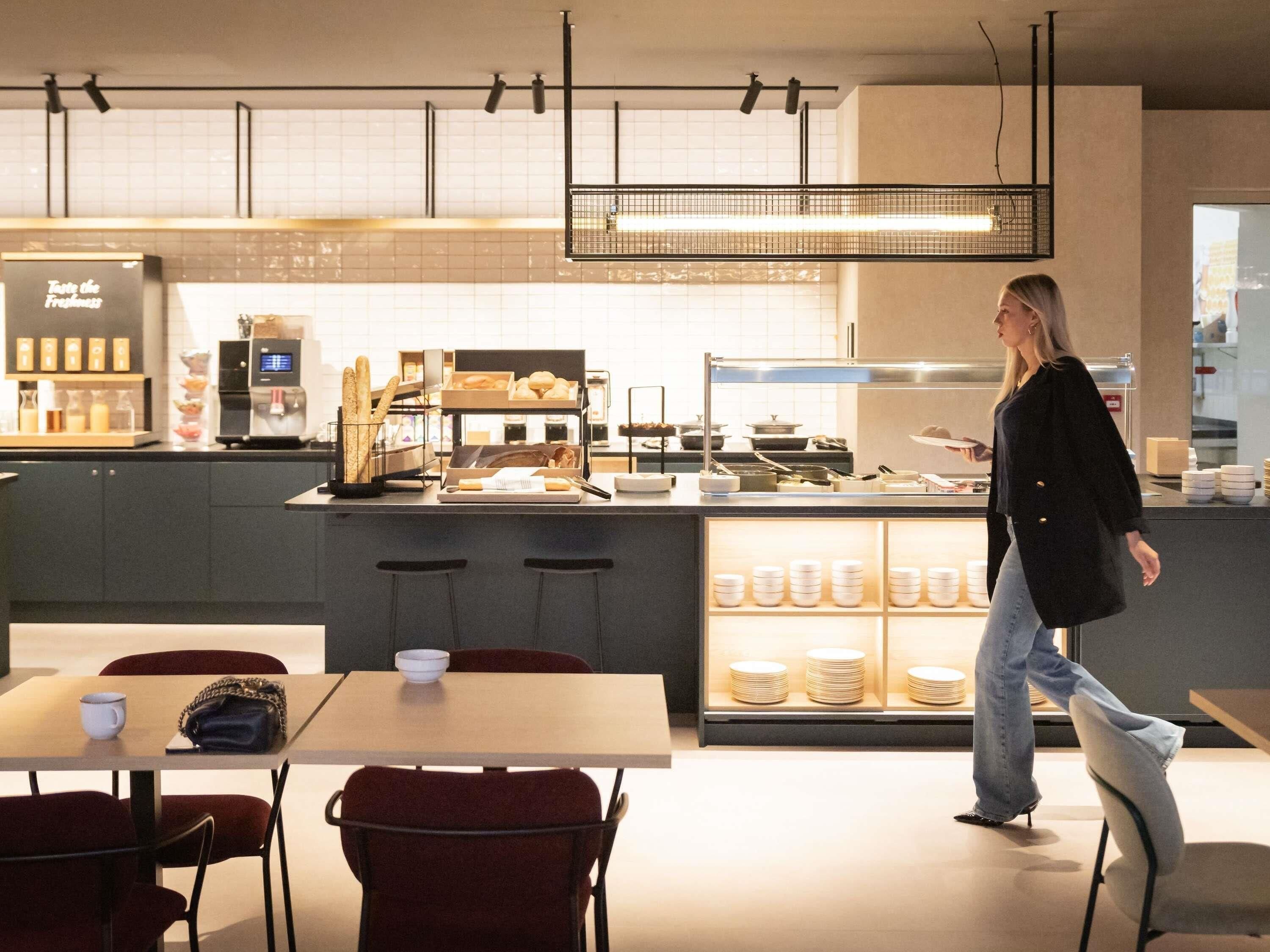 L’intérieur d’un café moderne, avec un comptoir, un espace salon et une personne qui marche.