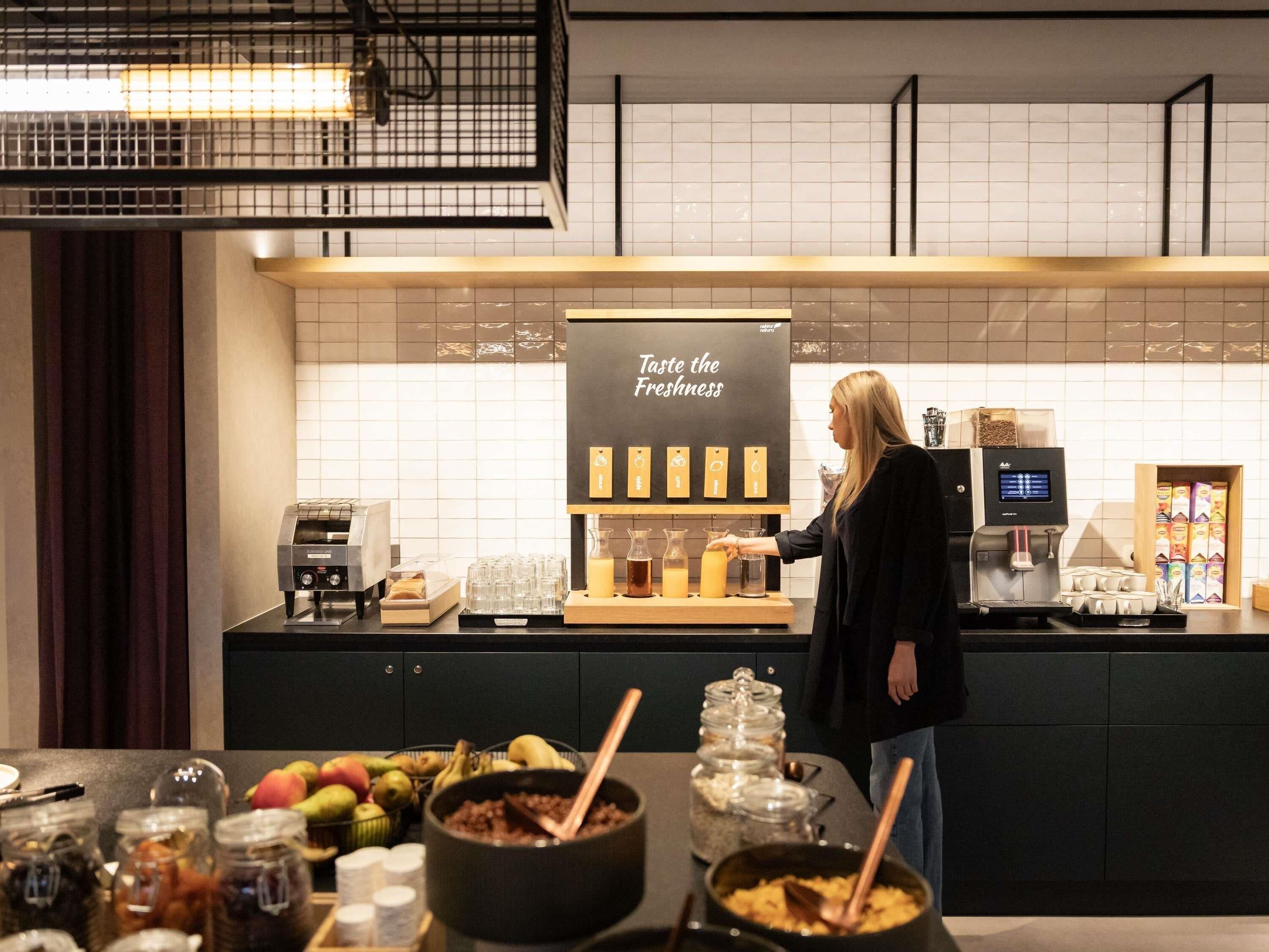 En person står vid en kaffestation med en skylt som lyder: ”Smaka på den friska smaken”. På disken finns olika sorters mat och en kaffemaskin.