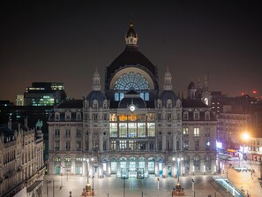 Um edifício grande e histórico com uma cúpula imponente e várias torres, rodeado por uma praça ampla com uma fonte.