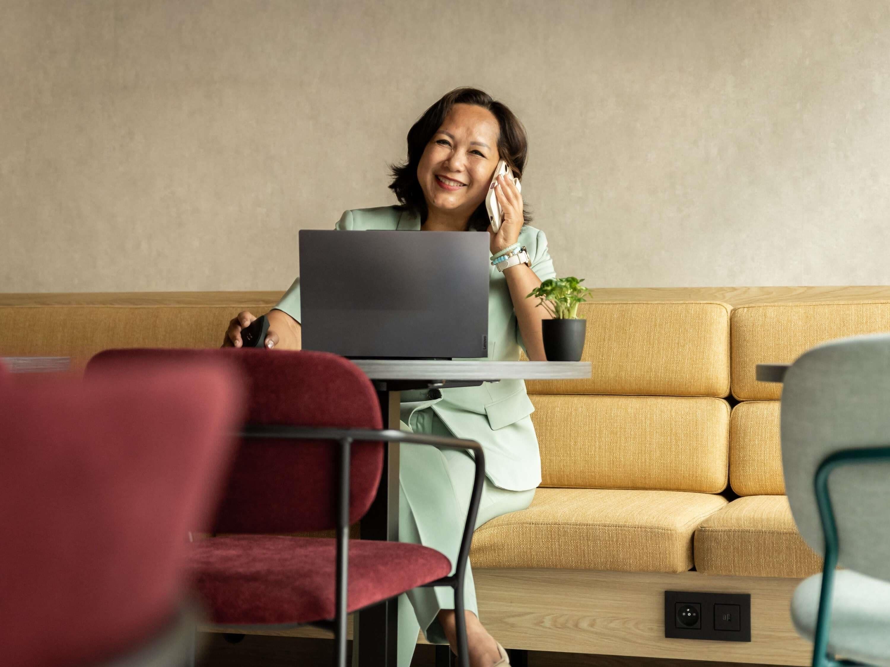 A person sitting at a table with a laptop, a plant, and a smartphone.