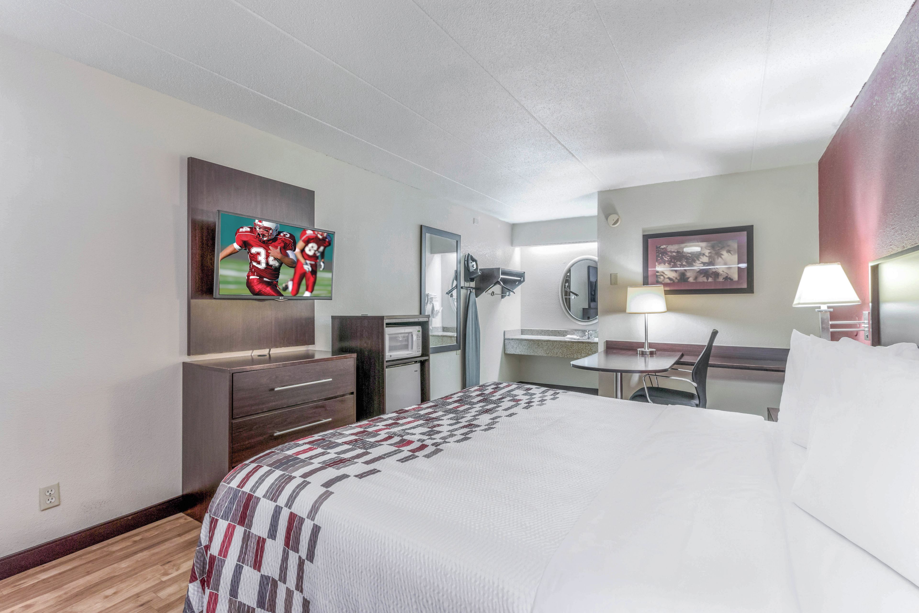 A hotel room with a bed, a desk, a chair, a television, a microwave, and a mirror.