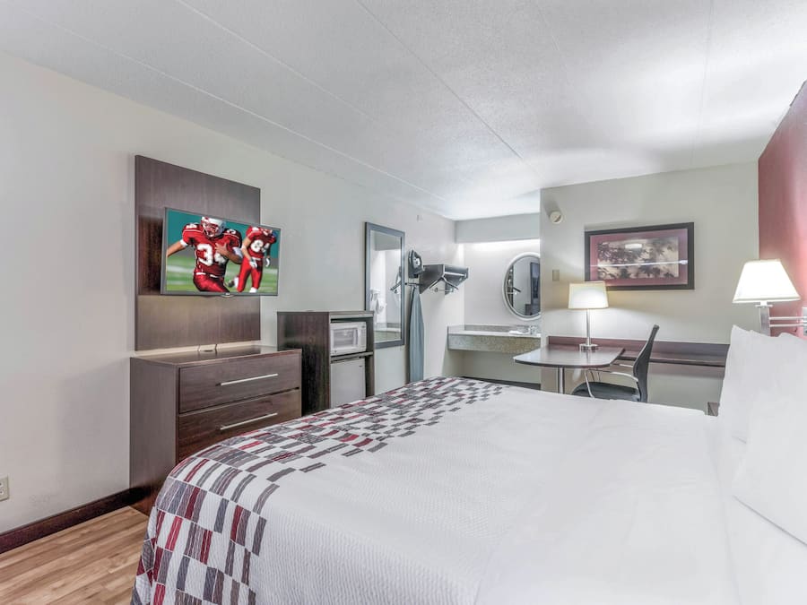 Een hotelkamer met een bed, een bureau, een stoel, een televisie, een magnetron en een spiegel.