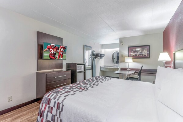 A hotel room with a bed, a desk, a chair, a television, a microwave, and a mirror.