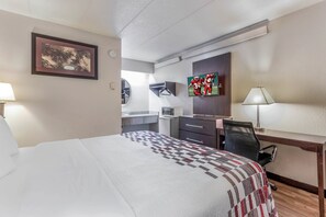 Quarto de hotel com cama, escrivaninha, cadeira, televisão e um quadro na parede.