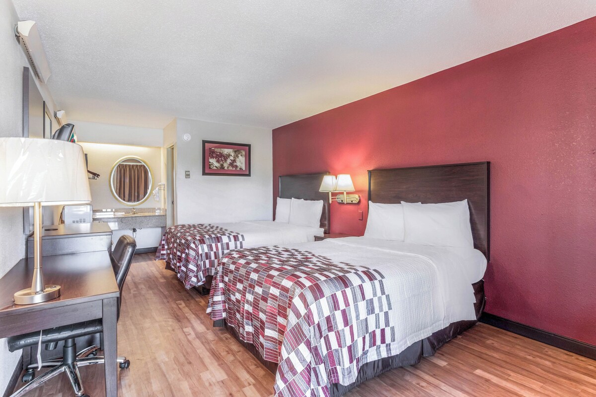 A hotel room with two beds, a desk, a chair, a lamp, and a mirror.