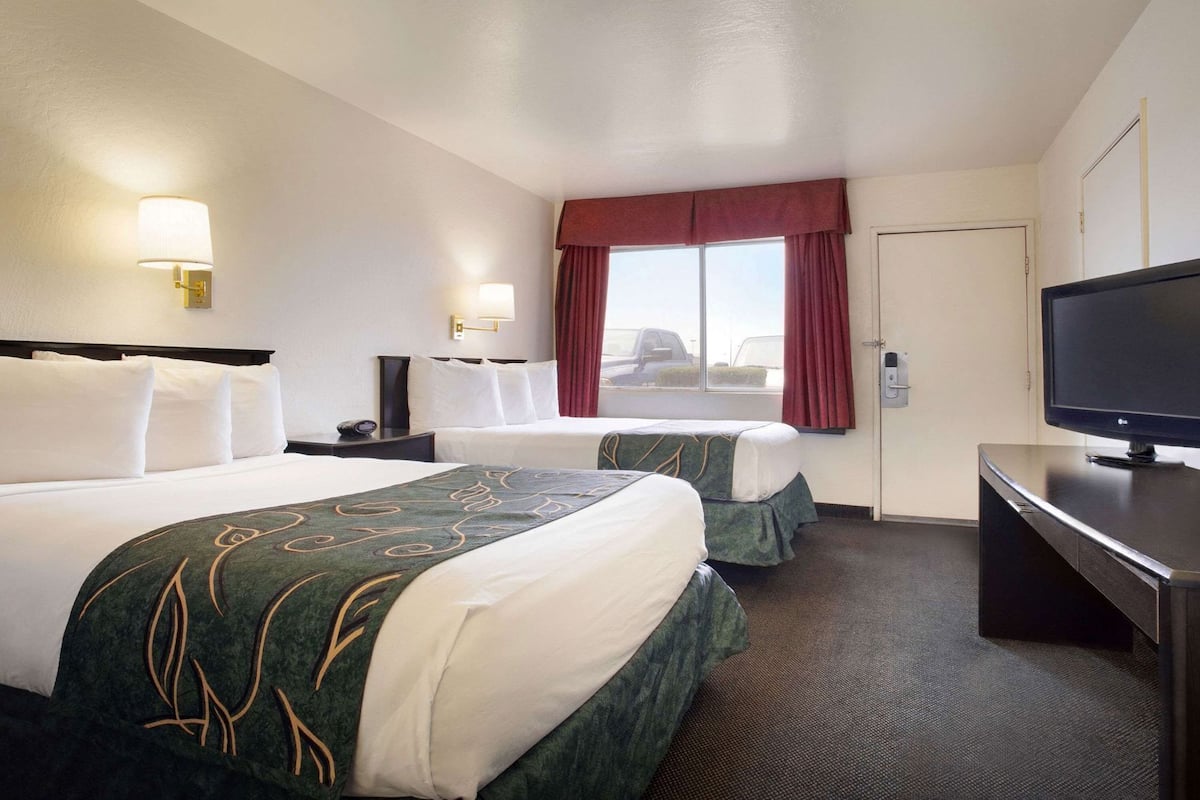 Une chambre d’hôtel avec deux lits, une télévision, un bureau et une fenêtre avec des rideaux.