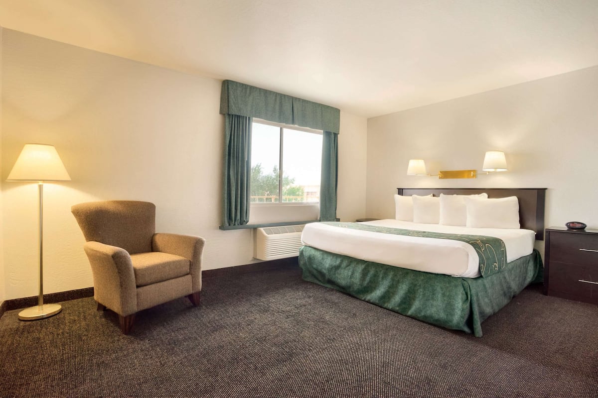Une chambre d’hôtel avec un lit, une chaise, une fenêtre avec des rideaux et une lampe.