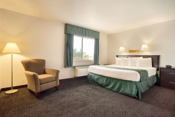 A hotel room with a bed, a chair, a window with curtains, and a lamp.
