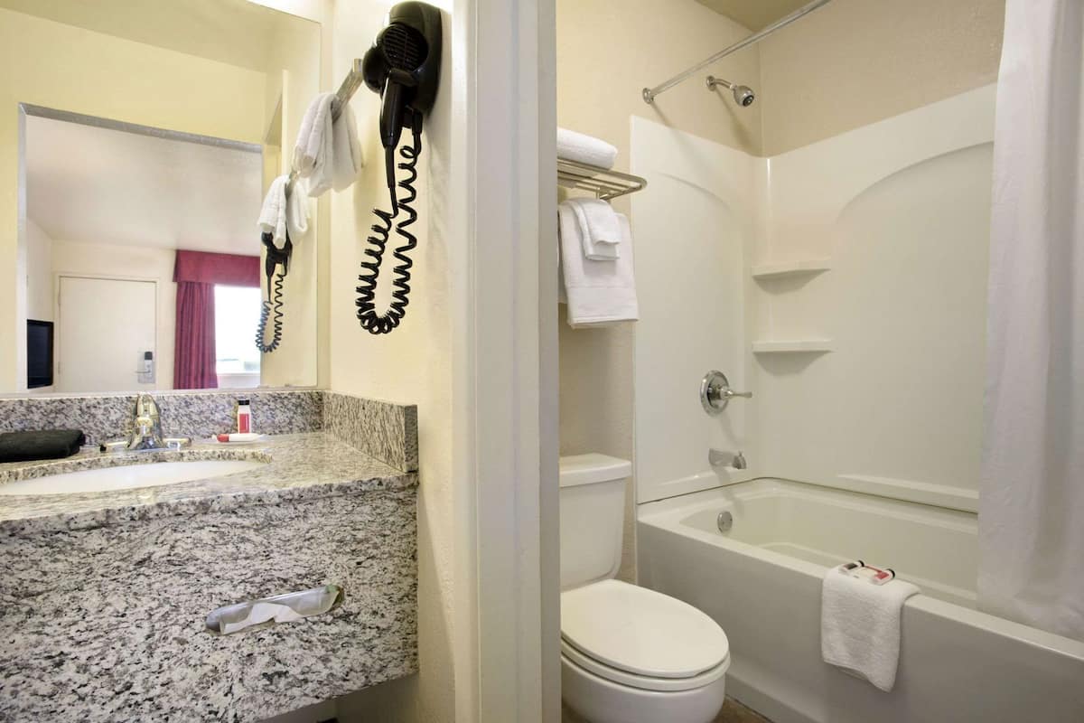 Une salle de bain dotée d’un comptoir en granit, d’un sèche-cheveux, de toilettes et d’une baignoire.