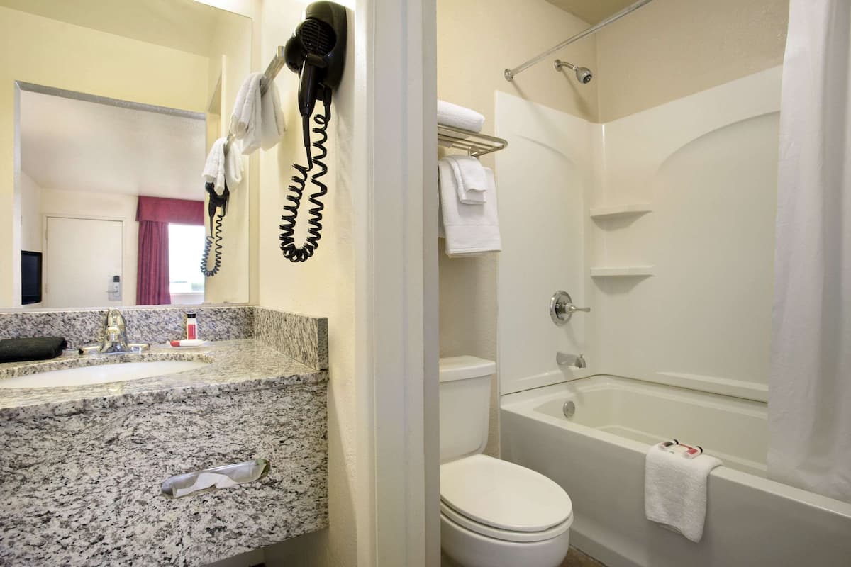 Une salle de bain avec un comptoir en granit, des toilettes blanches, une baignoire et un sèche-cheveux fixé au mur.