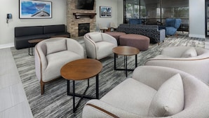 A modern living room with a stone fireplace, comfortable seating, and a large TV mounted on the wall. - Four Points by Sheraton Kansas City Airport (Kansas City)