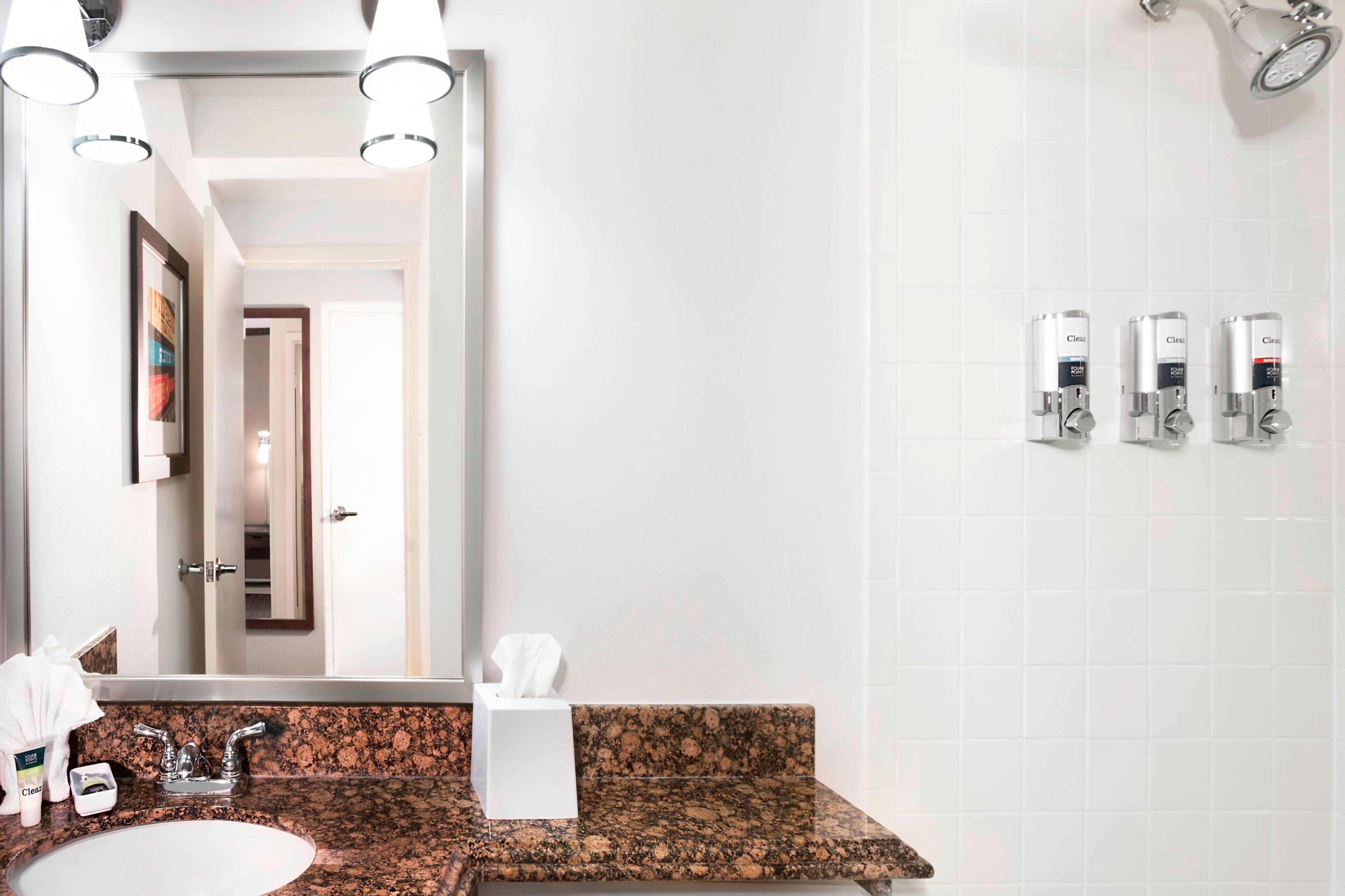 A bathroom with a granite countertop sink, a mirror, and three hand dryers on the wall.