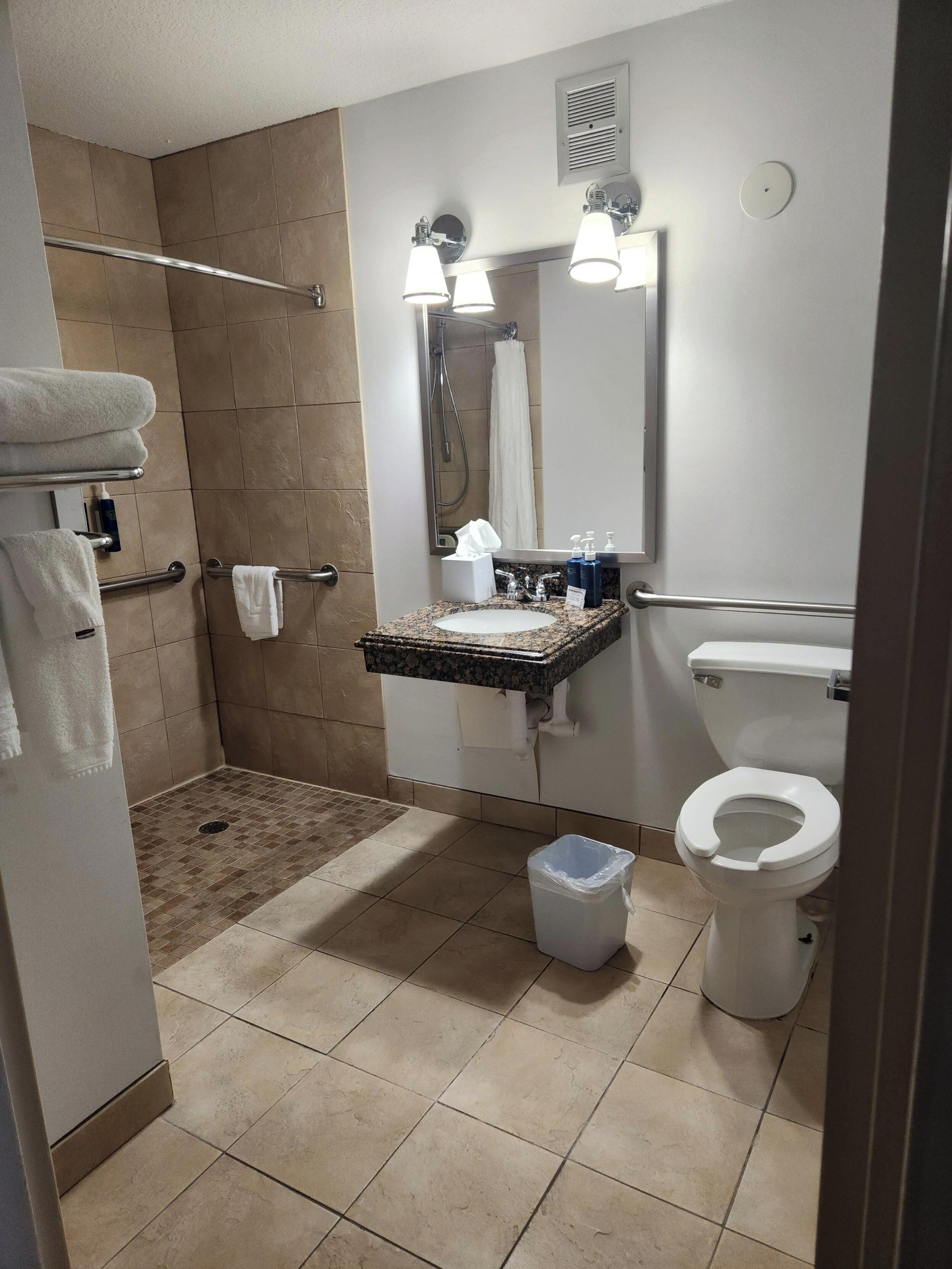 A bathroom with a shower, toilet, sink, and towel rack.
