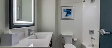A modern bathroom with a white sink, mirror, toilet, and bathtub.