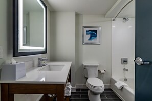 A modern bathroom with a white sink, mirror, toilet, and bathtub.