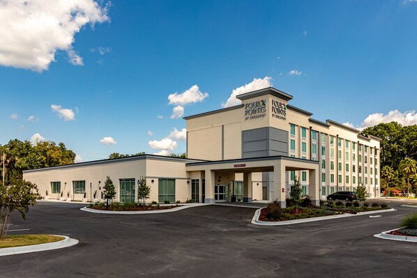 A hotel with a modern design, featuring a large entrance, multiple windows, and a parking lot.