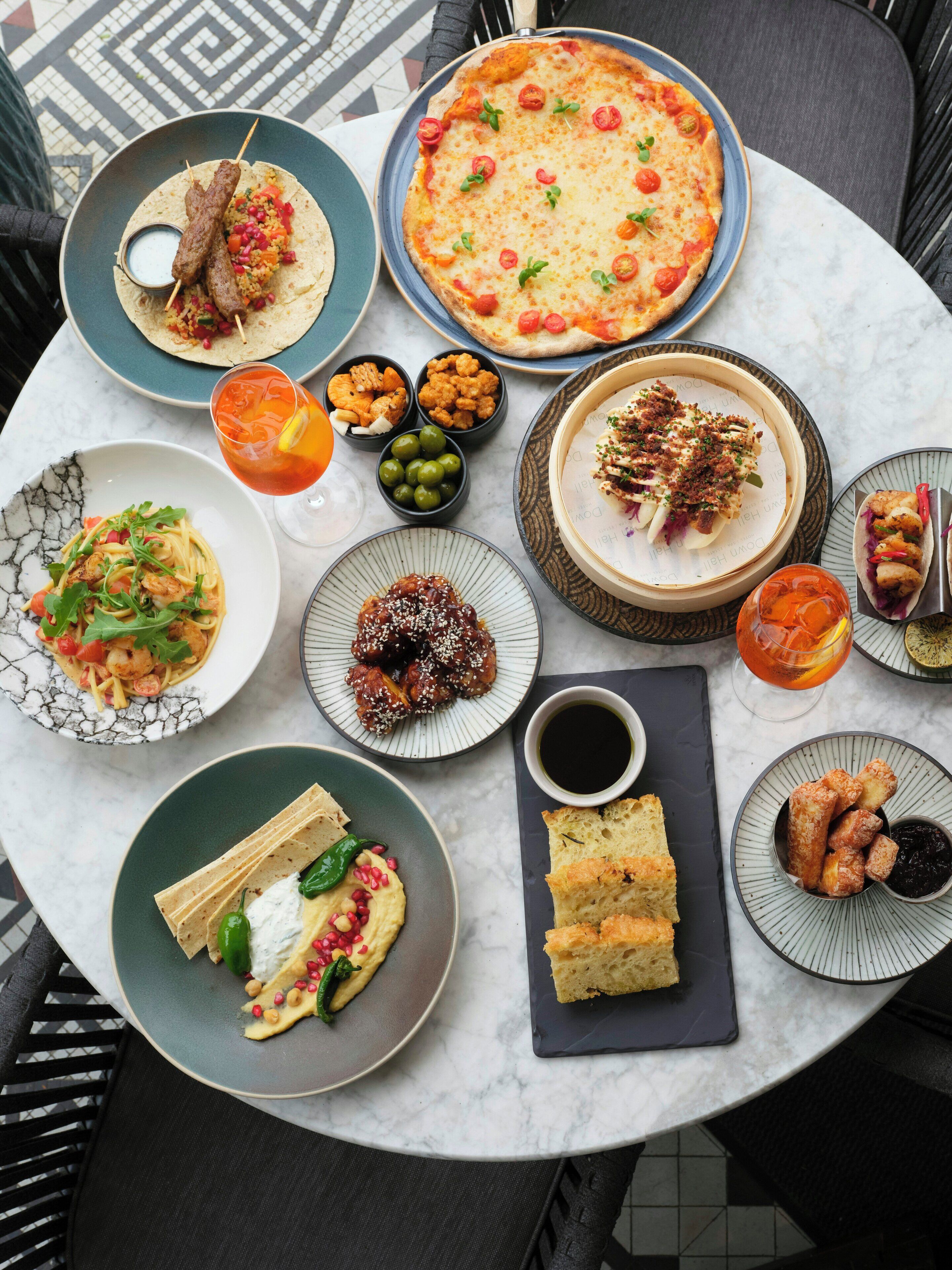 A variety of dishes and drinks on a round table, including pizza, tacos, and a salad.