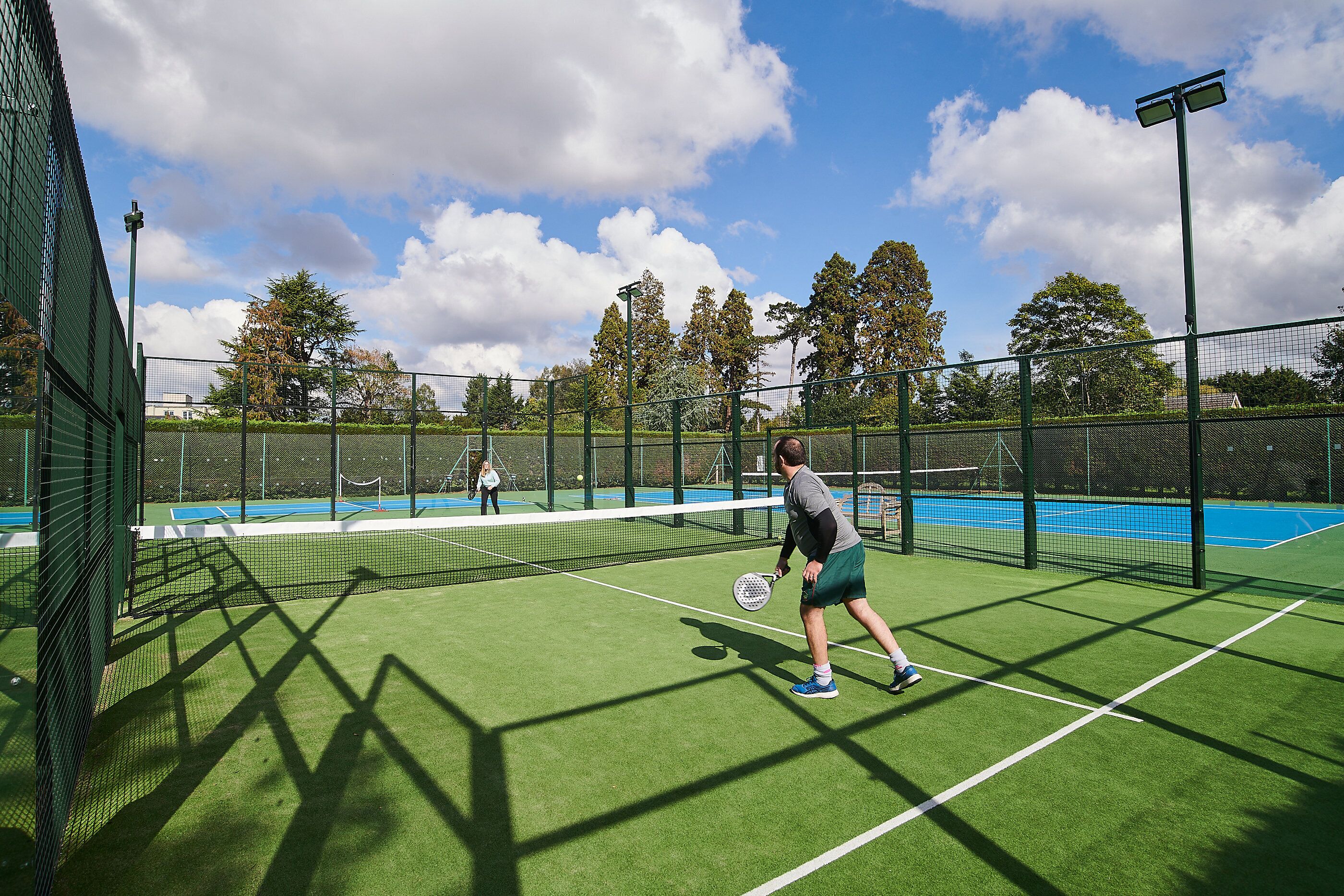 A tennis court with a net, green surface, and surrounding fence.