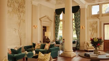 A spacious lobby with a green sofa set, a round coffee table, and a large vase with flowers.