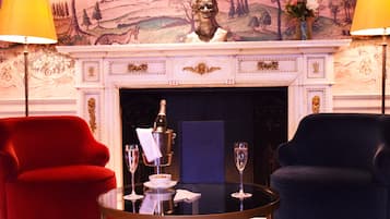 A room with a fireplace, two armchairs, a table with a bottle and glasses, and a decorative wall mural.