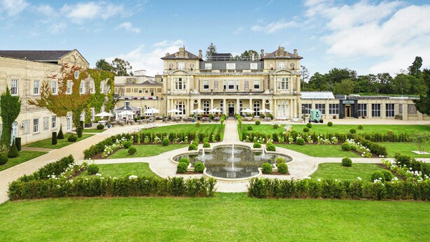 A large, historic building with a formal garden and a central fountain.