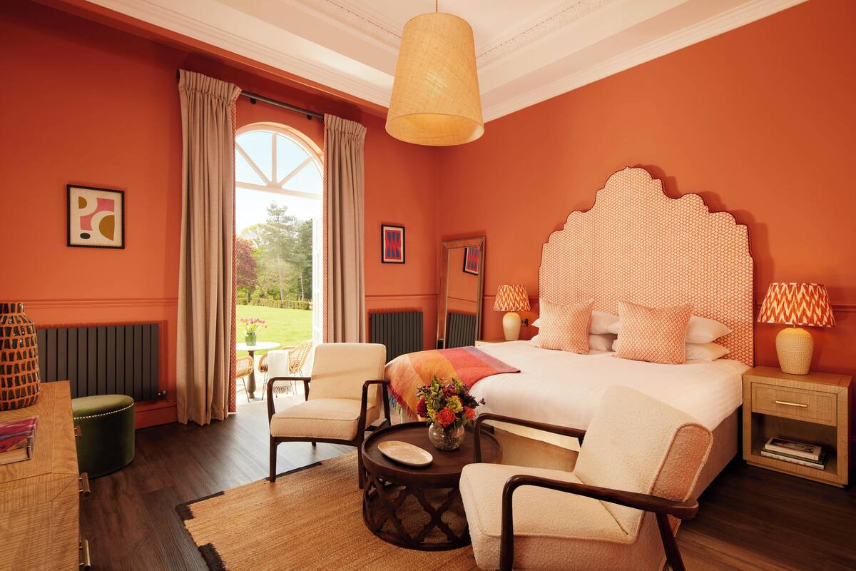 Une chambre à coucher avec un grand lit, deux chaises, une petite table ornée d’un vase de fleurs et une table de chevet avec une lampe.