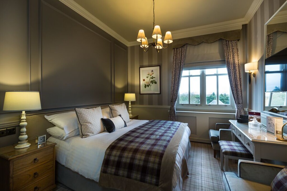 A hotel room with a large bed, bedside tables, a desk, a chair, and a window with curtains.