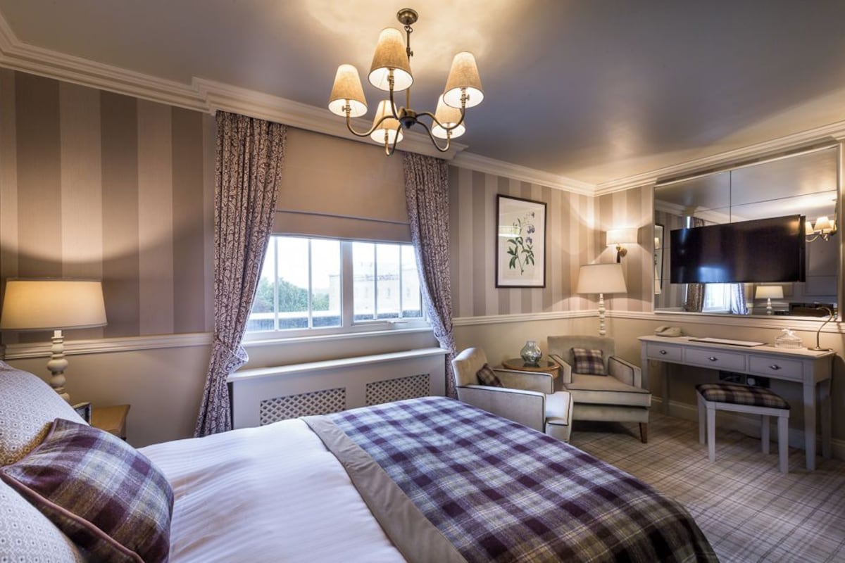 A hotel room with a bed, a desk, a chair, a television, and a window with curtains.