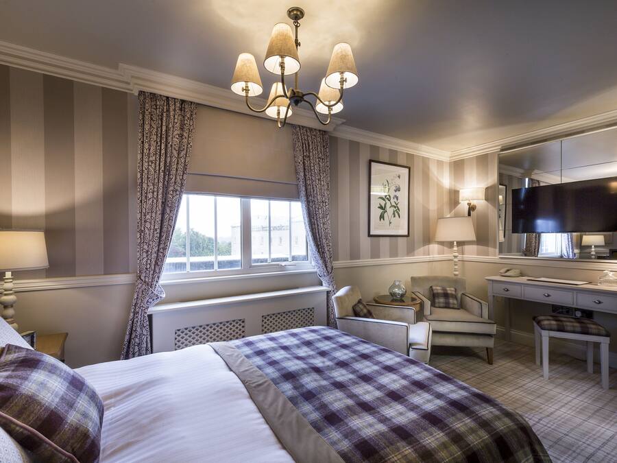Ein Hotelzimmer mit Bett, Nachttisch, Lampe, Stuhl, Schreibtisch, Fernseher und Vorhängen.