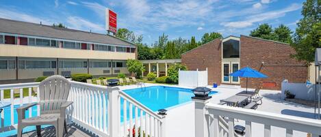 A swimming pool with a deck, a chair, and a table with an umbrella.