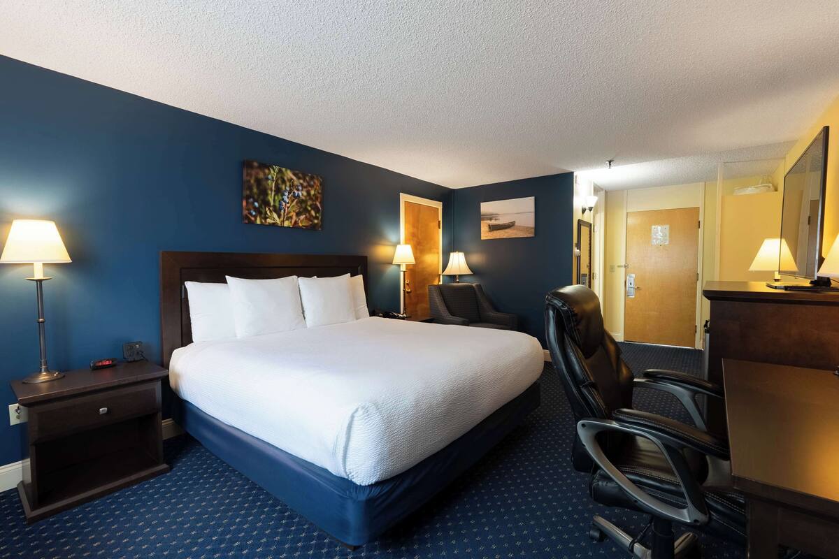 A hotel room with a large bed, two bedside lamps, a desk with a chair, and a mirror.