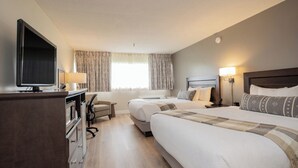 A hotel room with two beds, a TV, a desk, and a chair.