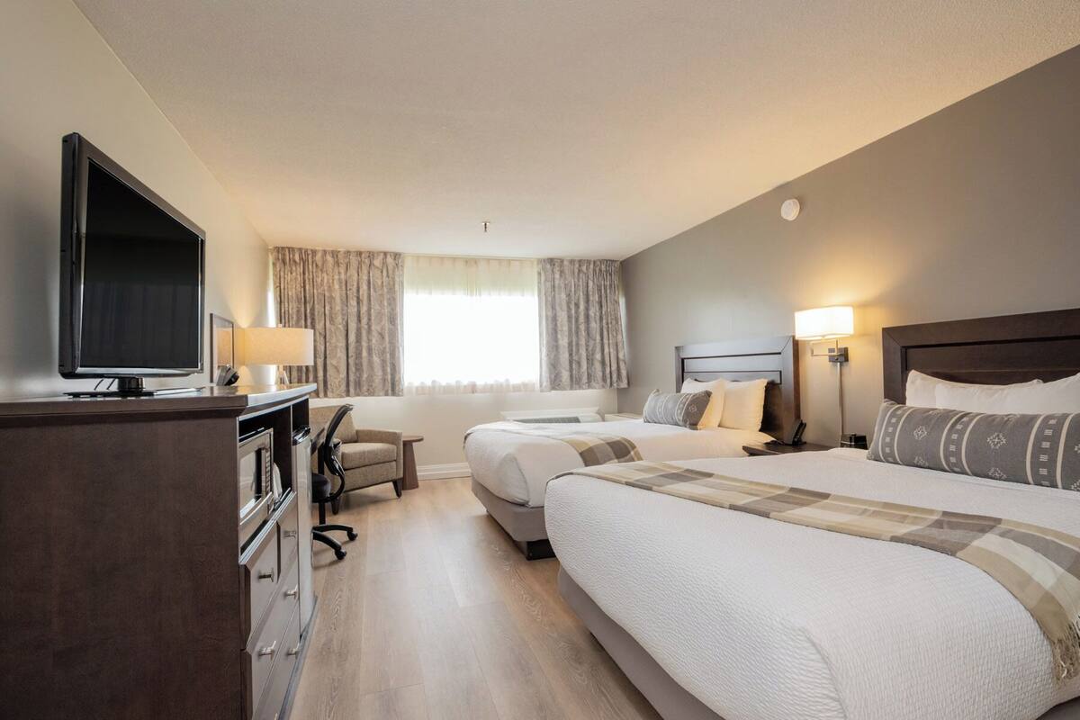 A hotel room with two beds, a TV, a desk, and a chair.